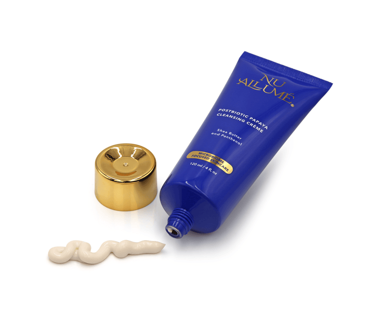 An open tube of Nu Allumé Postbiotic Papaya Cleansing Creme with some of the creme squirted onto the surface to demonstrate its colour and texture.
