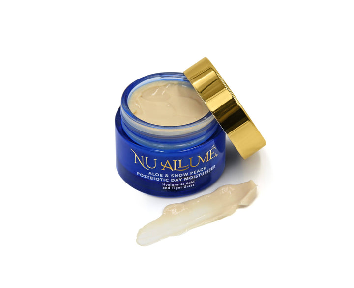 An open jar of Nu Allumé Aloe and Snow Peach Postbiotic Day Moisturiser with a smear of the moisturiser on the surface demonstrating its colour and texture