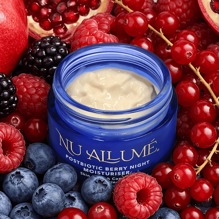 An open jar of Nu Allumé Postbiotic Berry Night Moisturiser surrounded by cranberries, blueberries, raspberries and pomegranate 