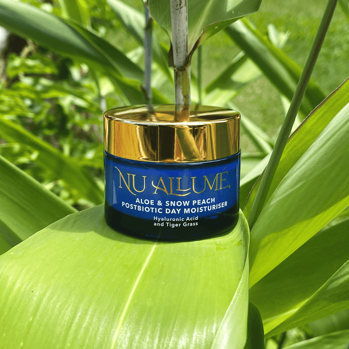A jar of Nu Allumé Aloe and Snow Peach Postbiotic Day Moisturiser Surrounded by Tiger Grass